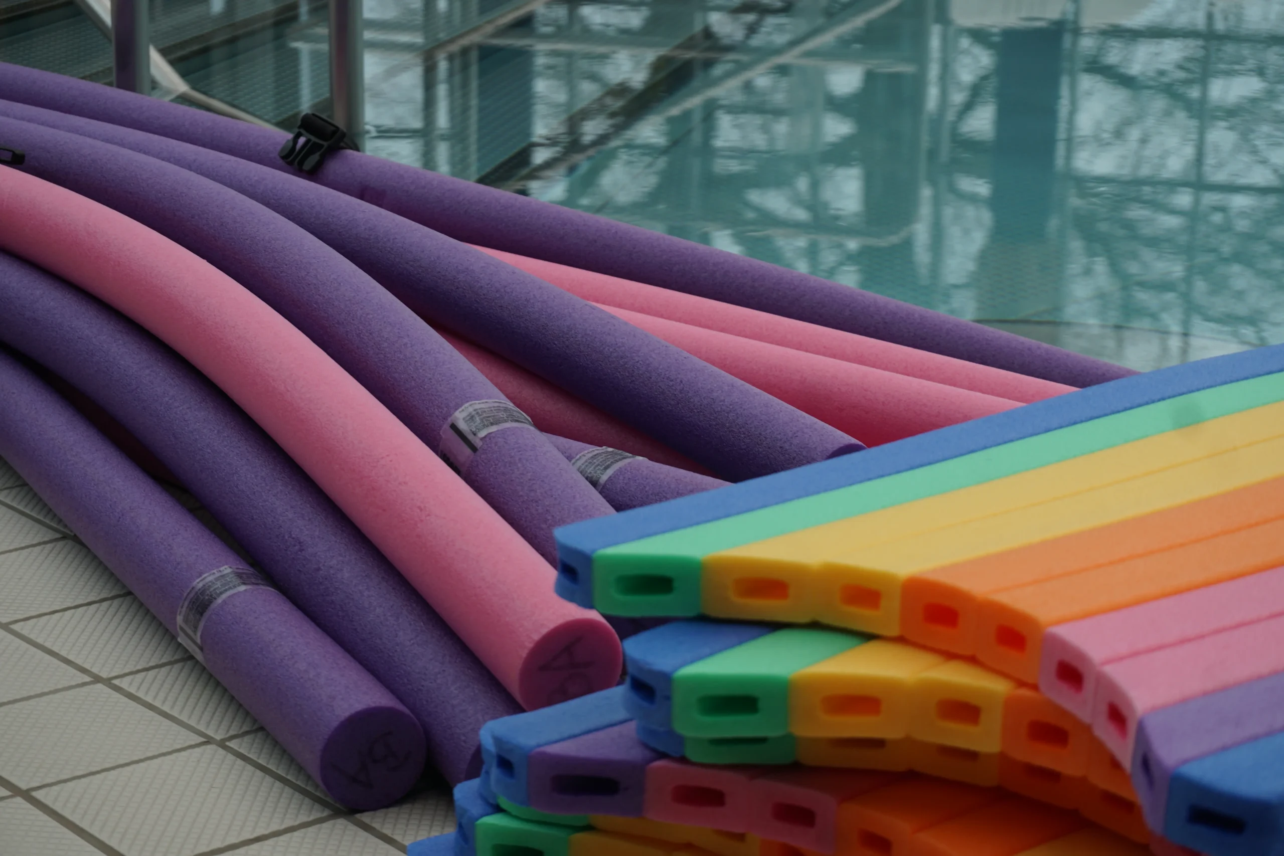 Schwimmnudeln und bunte Schwimmbretter am Beckenrand